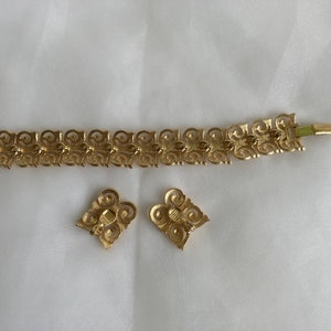 May include: A gold-tone bracelet and earrings set with a delicate, intricate design. The jewelry features a repeating pattern of swirls and loops.