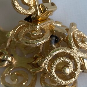 May include: Gold-toned metal bracelet with a detailed, intricate design. The bracelet has a clasp closure.