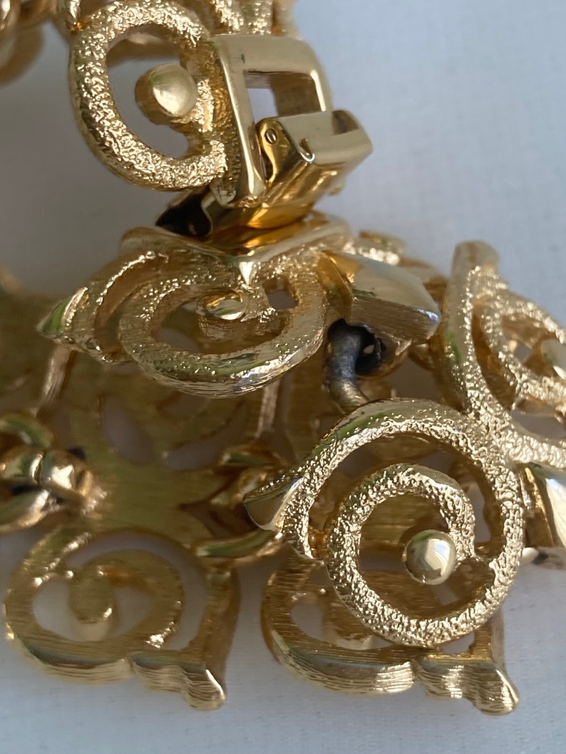 May include: Gold-toned metal bracelet with a detailed, intricate design. The bracelet has a clasp closure.