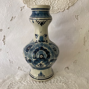 Puede incluir: Un jarrón de cerámica blanca con un diseño floral azul y blanco. El jarrón tiene una base ancha y un cuello estrecho.