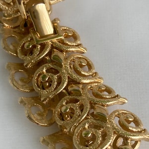 May include: Gold-tone bracelet with a detailed, intricate design of swirling, interconnected circles and loops. The bracelet has a secure clasp.
