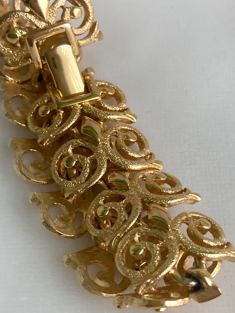 May include: Gold-tone bracelet with a detailed, intricate design of swirling, interconnected circles and loops. The bracelet has a secure clasp.