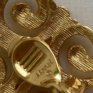 May include: Gold-toned metal earrings with a swirl design. The back of the earrings are marked with the word "Monet" and a copyright symbol.