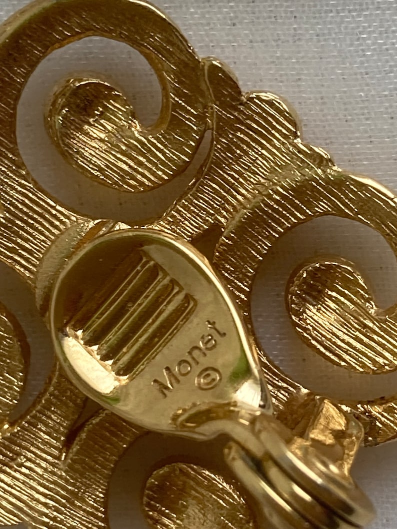 May include: Gold-toned metal earrings with a swirl design. The back of the earrings are marked with the word "Monet" and a copyright symbol.