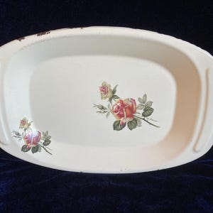 Op de afbeelding: Witte ovale ovenschaal met een bloemenmotief met roze en gele rozen. De schaal heeft een licht verweerde uitstraling.