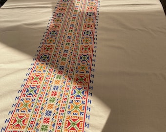 Può includere: Tovaglia bianca con un runner ricamato colorato con motivi geometrici in rosso, blu, verde, arancione e giallo.