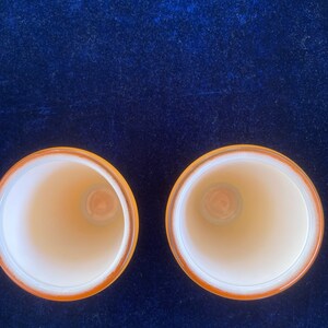 May include: Two empty, white ceramic cups with a yellow rim, sitting on a dark blue velvet surface.