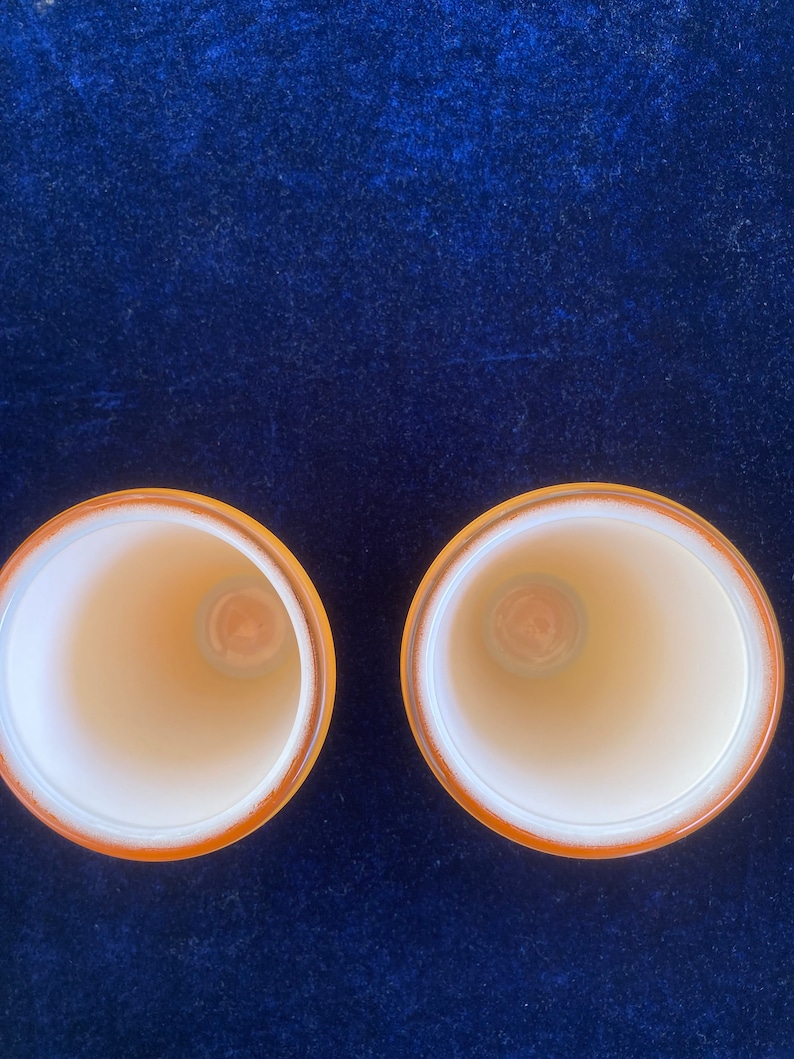 May include: Two empty, white ceramic cups with a yellow rim, sitting on a dark blue velvet surface.