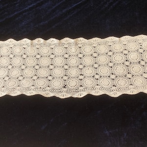 May include: A white crocheted table runner with a scalloped edge and a repeating pattern of circles.