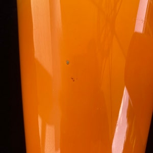May include: A bright orange glass vase with a smooth, shiny finish. The vase has a wide mouth and a narrow base.