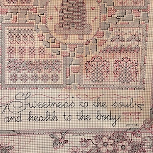 Może przedstawiać: Wzór haftu krzyżykowego z szczegółowym wzorem w odcieniach czerwieni, szarości i kremu. Wzór zawiera ul, wzory kwiatowe i cytat „Słodycz dla duszy i zdrowie dla ciała”. Widoczne jest również słowo „truskawka”.