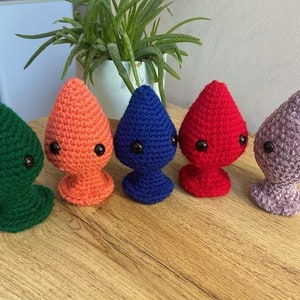 Könnte beinhalten: Fünf gehäkelte Plüschtiere in Tropfenform mit Glitz Augen. Die Spielzeuge sind grün, orange, blau, rot und lila.