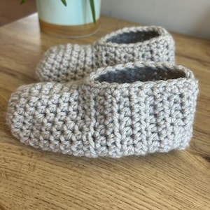 May include: A pair of gray crocheted slippers. The slippers are made with a simple stitch pattern and have a soft, cozy look.