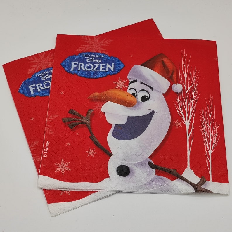 Puede incluir: Dos servilletas de papel rojas con borde blanco. Las servilletas presentan una imagen de dibujos animados de Olaf de la pel&iacute;cula de Disney Frozen. Olaf lleva un gorro de Pap&aacute; Noel rojo y sonr&iacute;e. El texto "From the movie Disney FROZEN" est&aacute; impreso en las servilletas.
