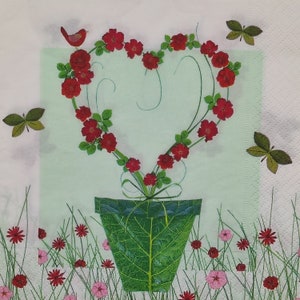 May include: A heart-shaped arrangement of red roses in a green pot with leaves. The roses are arranged in a circle around the pot, and the leaves are green and lush.