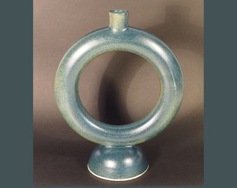 May include: A teal blue ceramic vase with a ring-shaped opening and a round base. The vase has a speckled finish.