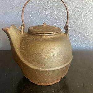 May include: A white ceramic mug with a black handle and the text "But First, Coffee" in a bold, black font. The mug is set against a blurred background, suggesting a cozy setting.