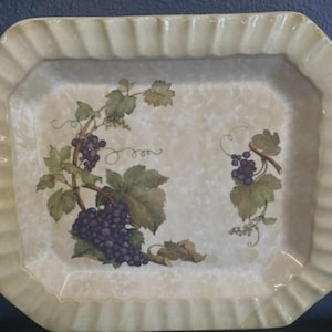 May include: Rectangular serving tray with a cream-colored, ruffled edge. The tray features a watercolor design of purple grapes, green leaves, and vines. The tray has an octagonal shape and is suitable for serving food.