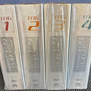 May include: Four DVD box sets of "Star Trek: The Next Generation" seasons 1, 2, 3, and 4. The DVD cases are silver with the show's logo and season number in red, orange, gold, and green. Each case is sealed in plastic.