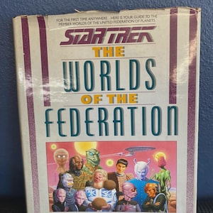 May include: A vintage book titled "Star Trek: The Worlds of the Federation." The cover features a colorful illustration of various alien species and the book's title in large, bold letters. The author's name, Shane Johnson, is also visible.