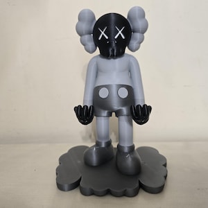 May include: A gray and black figurine of a cartoon character with a cloud-shaped base. The character has a black mask with white X's and a gray body with black shorts.