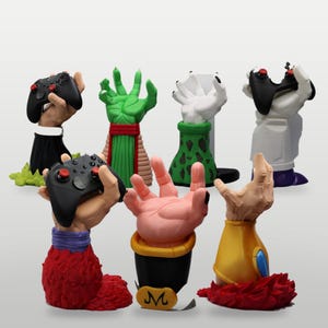 Può includere: Una collezione di sette supporti per controller a forma di mano scolpita, ognuno con colori e texture distinti ispirati a design di personaggi. Due supporti sostengono controller neri con levette rosse, mentre altri mostrano dettagli unici.