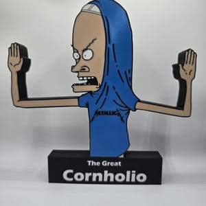 May include: A wooden figurine of the character Cornholio from the animated series Beavis and Butt-Head. The figure is wearing a blue shirt with the word "Metallica" and a blue hood. The base reads "The Great Cornholio."