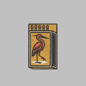 May include: Embroidered patch featuring a stylized heron in shades of red and brown, set against a mustard yellow background. The design is framed within a black border, resembling a matchbox. Six match heads are visible at the top.