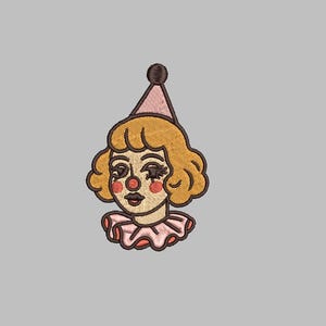 Puede incluir: Parche bordado con la cara de un payaso de estilo vintage. El payaso tiene el pelo rubio rizado, un sombrero rosa y un cuello con volantes. La cara del payaso tiene rubor rojo, una nariz roja y pestañas oscuras. Fondo gris.