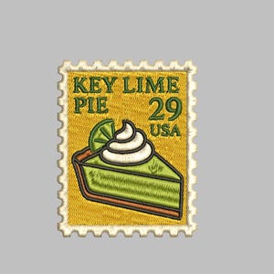 May include: Embroidered patch in the shape of a postage stamp. The stamp features a slice of key lime pie with whipped cream and a lime wedge. Text on the stamp reads "KEY LIME PIE 29 USA". The background is yellow with a scalloped border.
