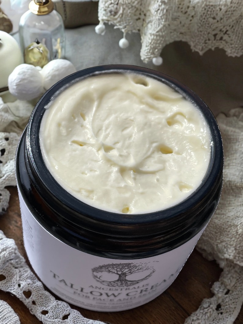 Peut inclure: Gros plan sur un pot en verre rempli d'une substance blanche et cr&eacute;meuse. Le pot a un couvercle noir et une &eacute;tiquette blanche qui indique "Ancestralis Tallow Cream for Face and Body".