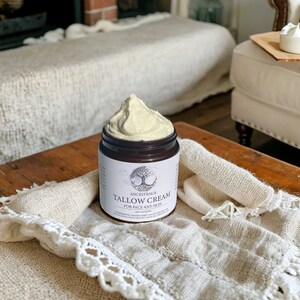 Peut inclure: Un pot de cr&egrave;me de suif Ancestralis pour le visage et le corps. Le pot est rempli d'une cr&egrave;me beige clair et repose sur une couverture en crochet blanc.