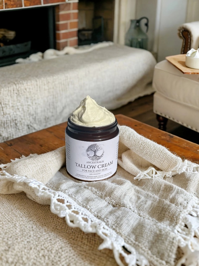 Peut inclure: Un pot de cr&egrave;me de suif Ancestralis pour le visage et le corps. Le pot est rempli d'une cr&egrave;me beige clair et repose sur une couverture en crochet blanc.