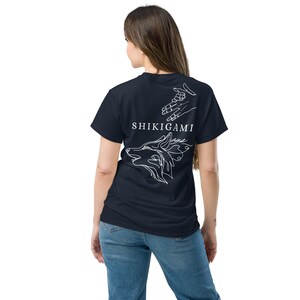 May include: A navy blue t-shirt with a white wolf head and hands design on the back. The text "SHIKIGAMI" is printed in white below the design.