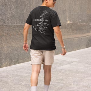 May include: A black t-shirt with a white graphic design of a wolf's head with flames and the text "SHIKIGAMI" on the back.