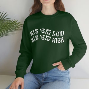 Pu&ograve; includere: Una felpa verde scuro con testo bianco che recita "Hit 'em Low Hit 'em High".