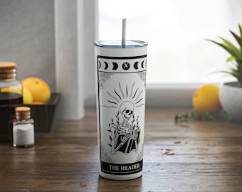 May include: White stainless steel tumbler with a black and white illustration of a skeleton reading a book. The tumbler has a black lid and a black straw. The text "THE READER" is printed on the tumbler.