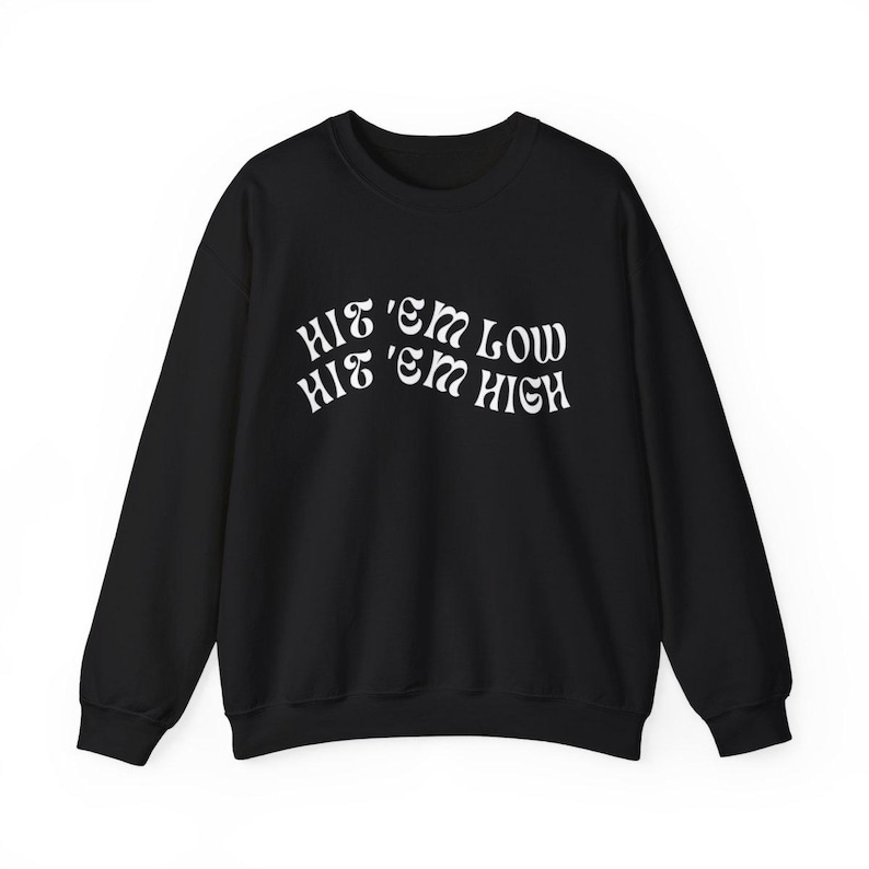 Pu&ograve; includere: Felpa nera con testo bianco che recita "Hit 'em Low Hit 'em High" in un font retr&ograve;.