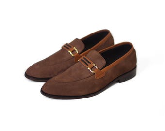 Könnte beinhalten: Braune Wildleder-Slipper mit goldener Schnalle und schwarzem Besatz. Die Slipper haben ein braunes Lederfutter.