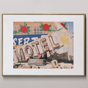 Peut inclure: Une photographie encadrée d'une enseigne de motel vintage avec le mot "MOTEL" en grandes lettres colorées. L'enseigne est partiellement effondrée et s'appuie contre un bâtiment. L'enseigne est entourée d'un paysage désertique.