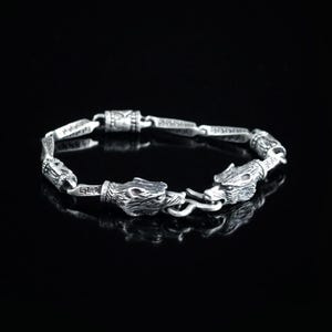May include: A silver bracelet with two wolf head charms. The bracelet is made of a chain with intricate details and a clasp.