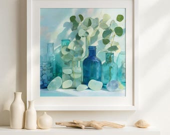 May include: A framed print depicting a still life of glass bottles in shades of blue and green. Eucalyptus branches are in some of the bottles. Smooth, pale blue stones are in front of the bottles. The artwork is in a white frame.