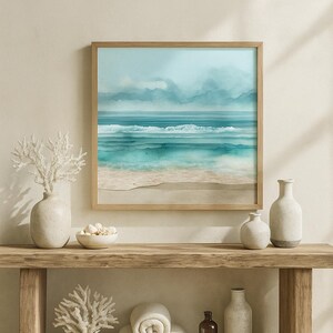 May include: A framed watercolour print depicting an ocean scene in shades of blue and white. It's displayed above a wooden console table with vases, a bowl of shells, rolled towels, and a small bottle. The overall aesthetic is coastal and serene, creating a calming atmosphere.