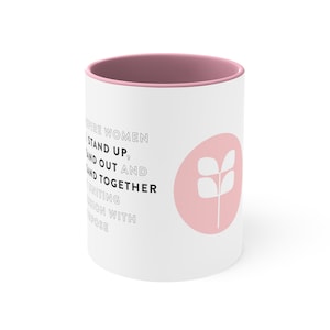 May include: White ceramic mug with a pink rim and a pink circle with a stylized plant design. The mug has the text "Inspire Women Stand Up, Stand Out and Stand Together Uniting Passion With Purpose" printed on the front.