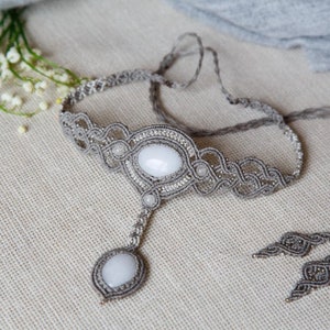 May include: A handmade gray macrame necklace with a central oval white stone pendant and matching earrings. The necklace features intricate knotwork and small bead accents, creating a delicate and bohemian aesthetic.