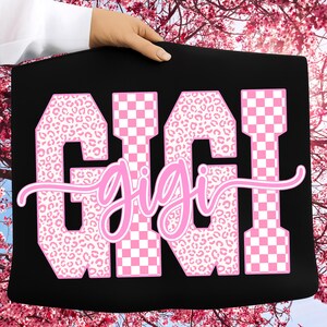 May include: Black tote bag with the name "GIGI" in large pink letters. The letters are a mix of leopard print and checkered patterns. The word "gigi" is written in a cursive font over the top of the letters.