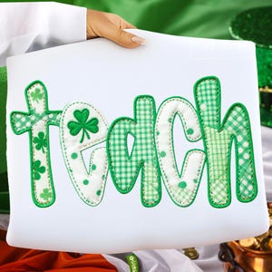 Puede incluir: Un letrero rectangular blanco con la palabra "teach" en letras de patchwork verdes y blancas. La letra "T" tiene acentos de trébol. Las letras son una mezcla de cuadros verdes, lunares y telas verdes lisas. El letrero lo sostiene una persona.