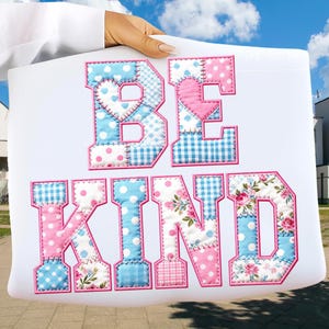May include: White tote bag featuring the words "BE KIND" in patchwork lettering. The letters are in blue and pink with polka dots, gingham, and floral patterns. The bag is held up against a blue sky.