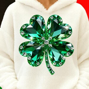 May include: A white hooded sweatshirt featuring a large, sparkling green shamrock design. The shamrock is made of faceted green gems with clear crystal accents, creating a dazzling effect. The design is centered on the chest of the soft, white hoodie.