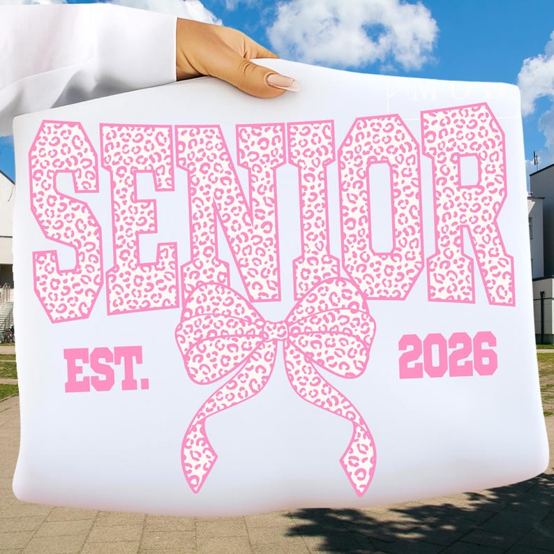 Puede incluir: Cartel blanco con texto rosa y dise&ntilde;o de lazo. La palabra "SENIOR" se muestra prominentemente, con un estampado de leopardo. Debajo, un lazo rosa. Tambi&eacute;n se ve el texto "EST. 2026".